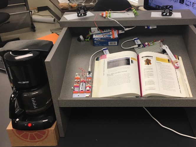 a littleBits construction sitting on a podium, attached to an open textbook; next to the podium is a coffee machine