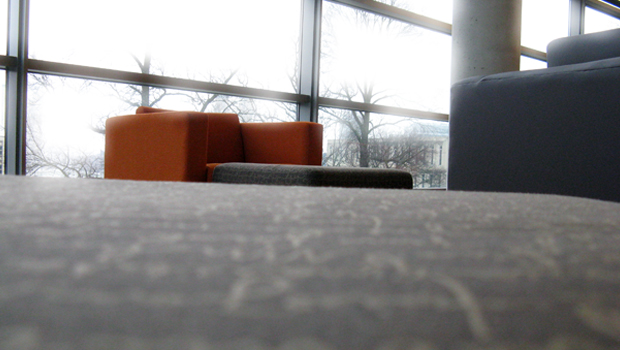 A red library chair sits toward the back of the photo. Leading up to the chair is a dark brown ottoman, which seems to stretch on forever.