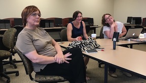 Joyce sits in the foreground, looking up toward an off-image television; Sarah and Erica look toward the camera, smiling