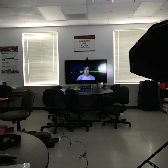 a view of a room with chairs and tables. At the far end of the room is a television monitor displaying an image of Joyce's head with a green sound wave in front of her face