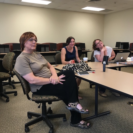 Joyce sits in the foreground, looking up toward an off-image television; Sarah and Erica look toward the camera, smiling