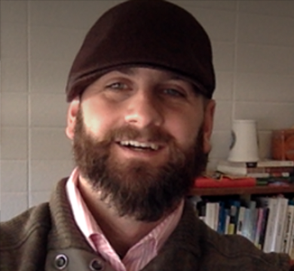 A headshot depicts a beareded and smiling Tim
                    wearing a brown hat