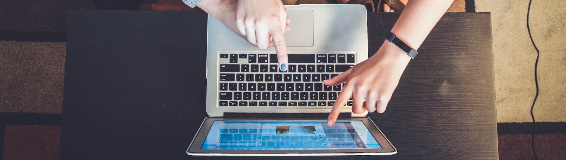 three hands hovering over a laptop, two pointing at the screen, the other on the mouse