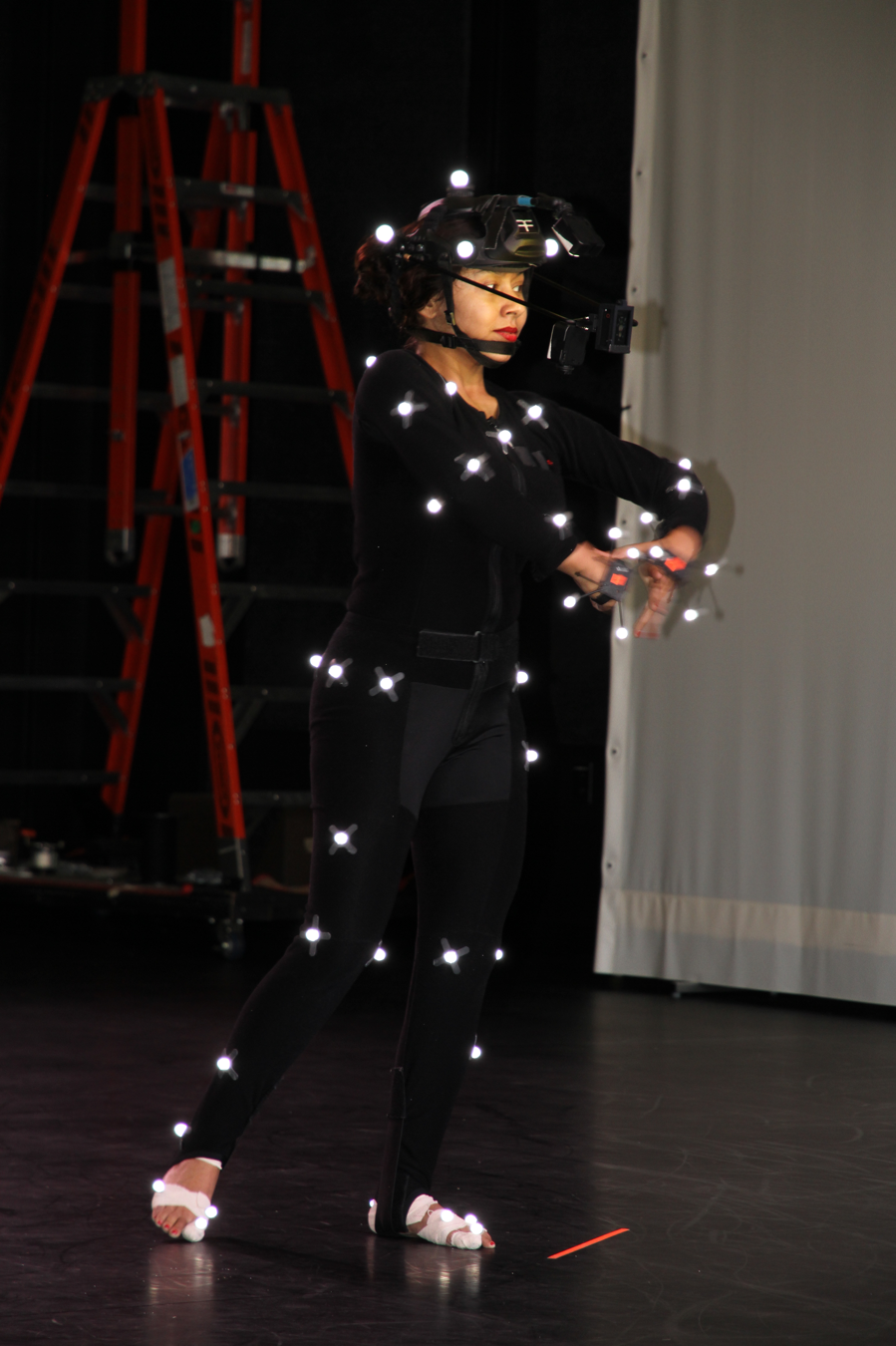 woman wearing black dancing; small lights are placed on limbs, waist, and head