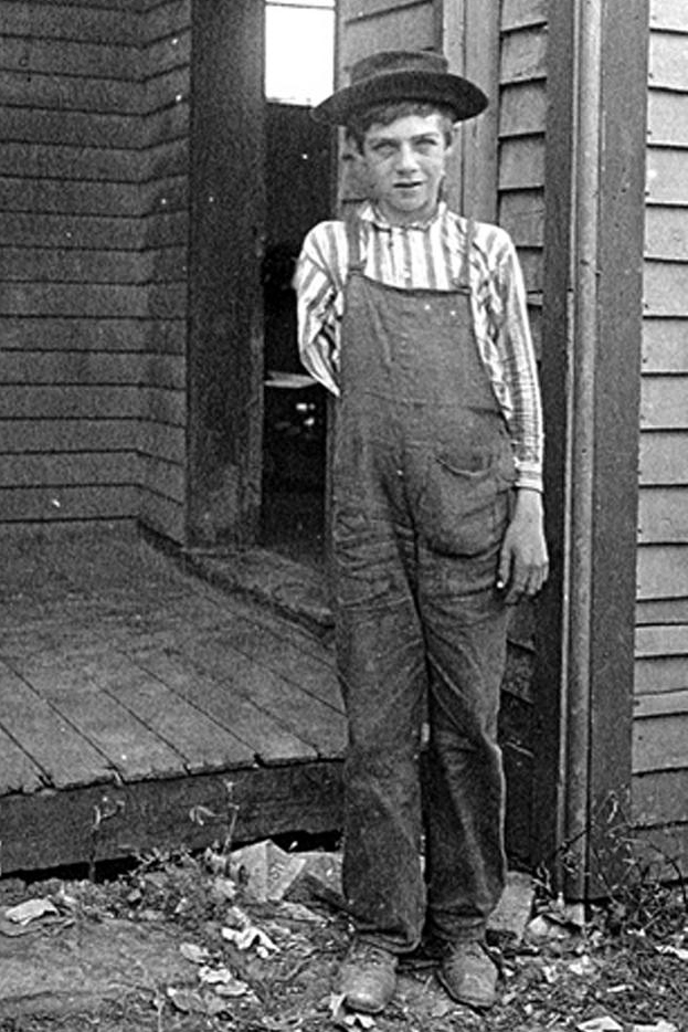 A black-and-white image shows a boy with a missing arm looking unsmiling into the camera.