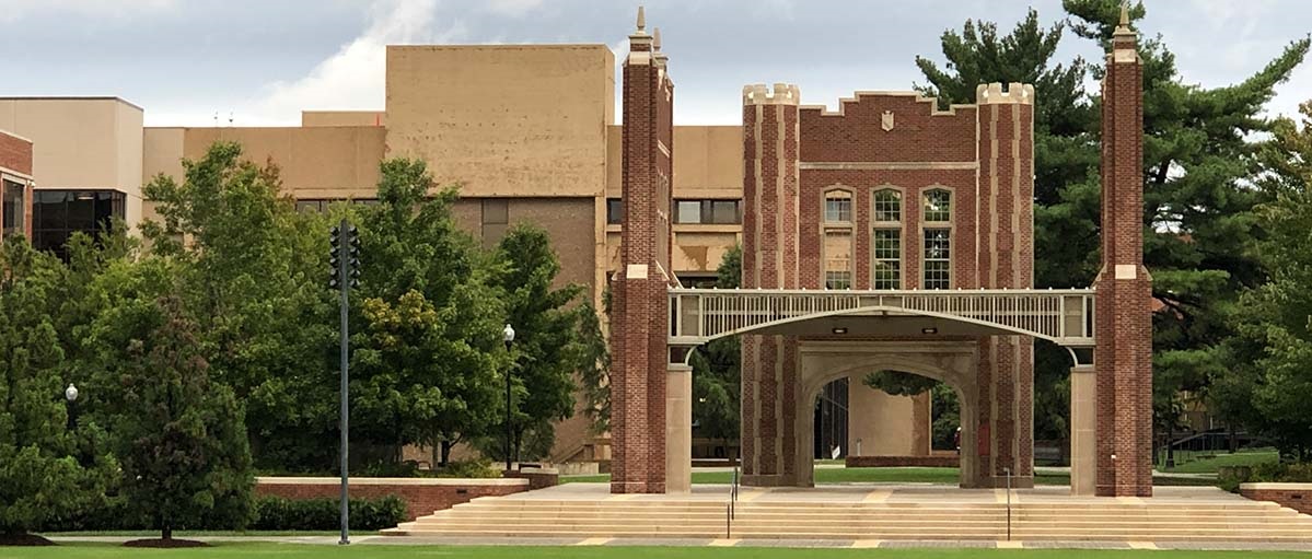 Chamberlain Arch: brown academic building with archway and steps on the right and plenty of trees on the left